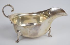 George V hallmarked silver sauce boat with shaped edge and scroll handle, raised on three pad