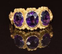 Victorian yellow metal ring set with three oval cut amethysts with floral decoration to the
