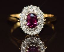An 18ct gold ring set with an oval cut ruby of approximately 0.5ct surrounded by diamonds, 4.4g,
