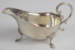 George V hallmarked silver sauce boat with shaped edge and scroll handle, raised on three hoof feet,