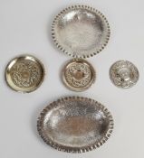 Five Iranian, Burmese or similar silver dishes, two with crimped edges raised on three feet each,