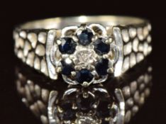 A 9ct white gold ring set with a diamond surrounded by sapphires, 3.8g, size M
