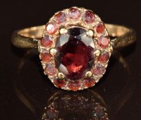 A 9ct gold ring set with an oval cut garnet surrounded by round cut garnets, 3.6g, size R