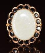 A 14k rose gold ring set with an oval cut opal cabochon surrounded by round cut sapphires, 8.4g,