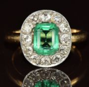 An 18ct gold ring set with a faux emerald surrounded by twelve transitional cut diamonds of