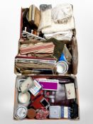 Three boxes containing table linen, tins, boxed cutlery, picture frames, etc.
