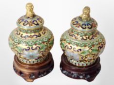 A pair of 20th century Chinese miniature cloisonné lidded urns with foo dog finials on hardwood