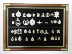 A montage of reproduction cap badges in brass-mounted frame, 69cm x 50cm overall.