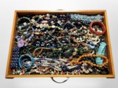 A wooden drawer containing assorted costume jewellery, bead necklaces, bracelets, etc.