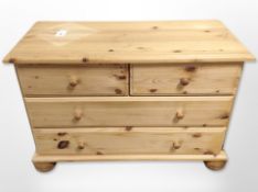 A contemporary pine four drawer low chest on bun feet,