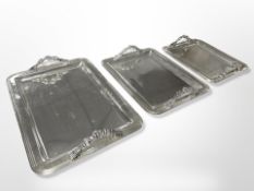 A graduated set of three silver-plated twin-handled serving trays with tasseled handles,
