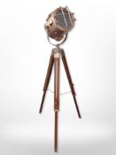A copper-effect spot lamp on wooden folding tripod, height 108cm.