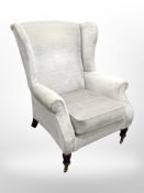 A Victorian style wing back armchair in pale blue upholstery, raised on brass castors,