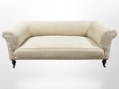 A Victorian style three seater settee in beige upholstery, raised on ceramic castors,