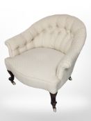 A late Victorian low tub armchair in buttoned upholstery, raised on ceramic castors,