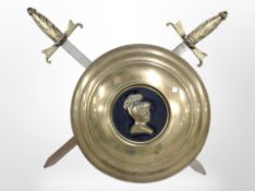 A decorative brass shield and crossed swords wall plaque, width 58cm.