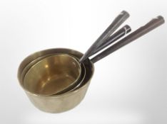 Three Victorian graduated brass and cast-iron sauce pans, largest 41cm long.