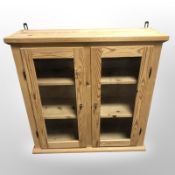 A contemporary pine glazed double-door wall cabinet, 81cm wide x 28cm deep x 79cm high.