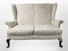 A reproduction wing-back two-seater settee, upholstered in floral fabric, width 133 cm.