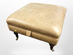 A reproduction tan leather storage stool on brass castors,