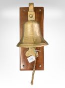A brass ship's bell mounted to mahogany back board,