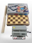 A vintage tin-plate adding machine, together with a chessboard with pieces,