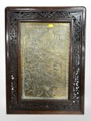 An oriental embossed brass plaque in carved hardwood frame, overall 58cm x 43cm.