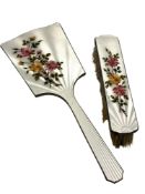 A three-piece floral enamelled and silver mirror and two brush set.