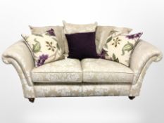A contemporary two seater settee in two-tone floral upholstery with scatter cushions retailed by