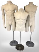 Three male mannequin torsos on stands