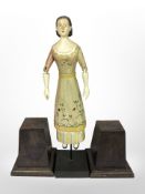 A folk art carved wooden figure of a lady with articulated arms, plus two further wooden plinths,