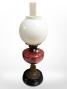 A brass oil lamp with cranberry glass reservoir and opaque shade, height 55cm.