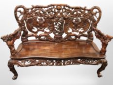 An oriental heavily carved hardwood three seater bench, with carved dragon arm rests,
