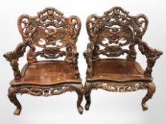 A pair of oriental heavily carved hardwood open armchairs with dragon arm rests,