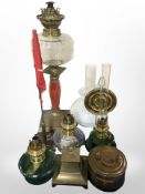 A brass oil lamp with clear glass reservoir and opaque shade, three further lamps,