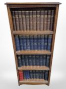 A carved oak open bookcase containing Dickens and other volumes,