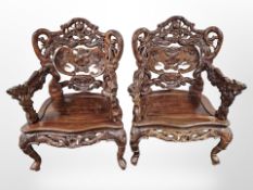 A pair of oriental heavily carved hardwood armchairs, with dragon arm rests,