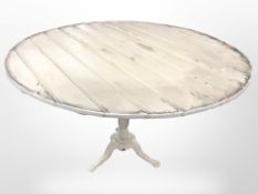 A distressed painted pine circular table on cast iron tripod support, diameter 95cm.