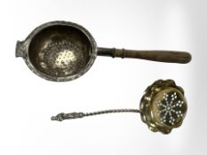 A silver strainer with turned wooden handle, together with a further plated straining spoon.