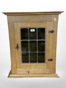 A 20th century blonde oak wall cabinet with stained and leaded glass door, 53 cm x 26 cm x 63 cm.