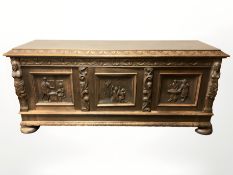 An early 20th century heavily carved oak triple door low sideboard on bun feet,