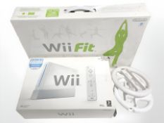 A Nintendo Wii console and Wii Fit board in boxes, two accompanying steering wheels.