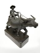 A contemporary oriental bronze statue on wooden plinth of a figure riding a water buffalo,
