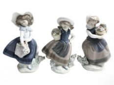 Three Lladro figures of girls carrying baskets of flowers, tallest 18 cm.