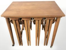 A nest of five teak stowaway tables on castors, with plate glass top, width 62 cm.