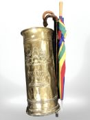 An embossed brass stick stand, height 61 cm, containing two walking sticks and an umbrella.