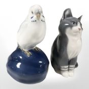 A Royal Copenhagen budgerigar perched on a fruit, and a further figure of a seated cat,