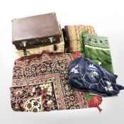 A wicker hamper, a small suitcase and a group of embroidered throws.