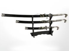A graduated set of three Eastern curved swords with cobra pommels, on ebonised sword stand,