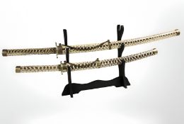 A pair of reproduction Japanese katanas in faux snake skin scabbards, on an ebonised sword stand,